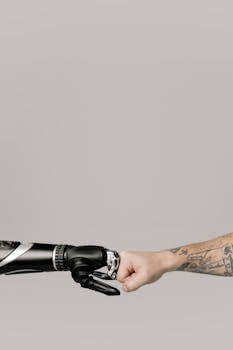 A human fist bumping with a prosthetic arm on a neutral background.