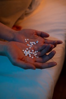 A person holding a handful of pills in a dimly lit bedroom, conveying themes of health and mental wellness.