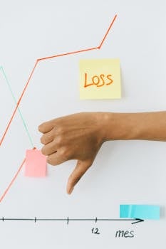 Hand showing thumbs down in front of graph indicating financial loss concept.