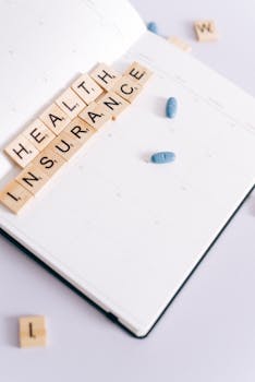 Scrabble tiles spelling 'health insurance' on a calendar beside blue pills, symbolizing medication schedule.